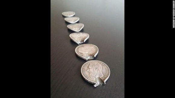 6 Belgian Coins that are lined up. These coins were shot with a bullet. Each coin has an indentation of a bullet.